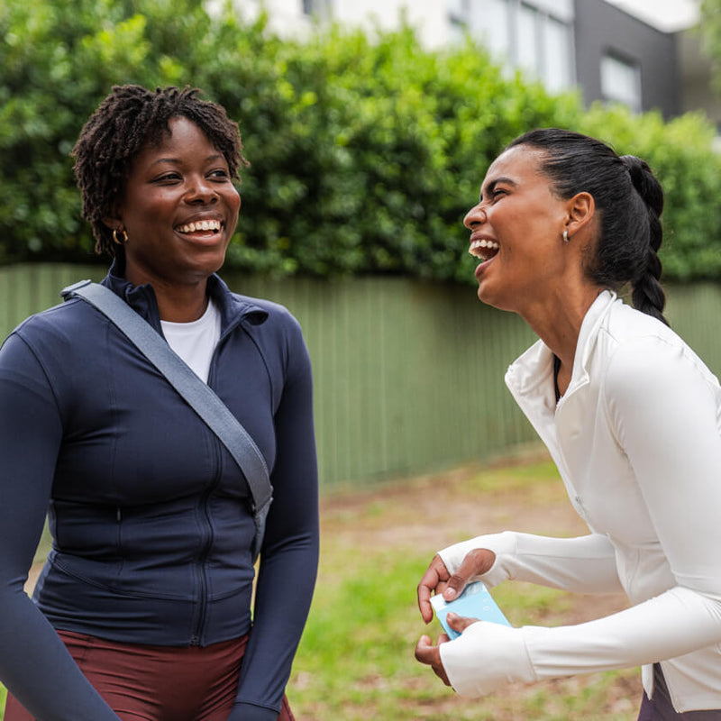 Two women laughing together outdoors with greenery in the background