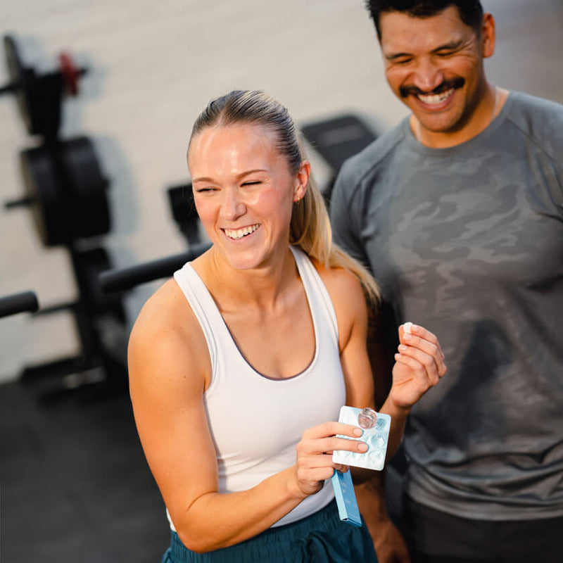 Woman smiling after a gym workout holding a supplement pack