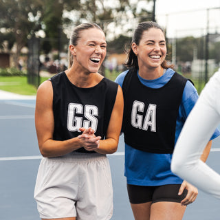 Two women in sports uniforms smiling on an outdoor court